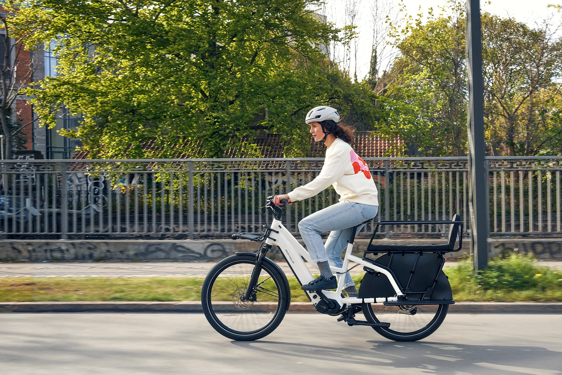 Symbolbild des Leasings für E-Bikes bei Rückenwindräder in Wilhelmshaven: Eine Frau sitzt mit Fahrradhelm auf einem weißen E-Bike und fährt auf einer Straße von rechts nach links durchs Bild.